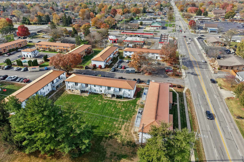 Aerial view of suburban neighborhood with orange-roofed apartments, parking lots, main road, and autumn trees at Charleston Square Apartments in Columbus, Indiana