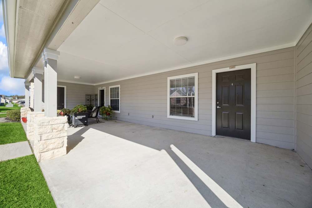 Covered front porch with black doors, windows, outdoor furniture, and potted plants at Palm Garden in Orange, Texas
