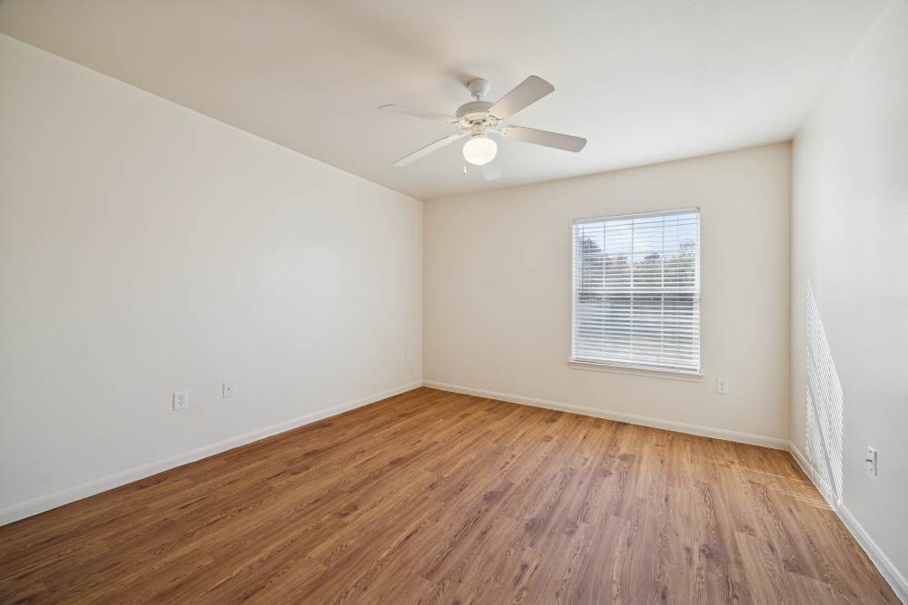Unfurnished bedroom with wooden flooring , large window and ceiling fan at Palm Garden in Orange, Texas