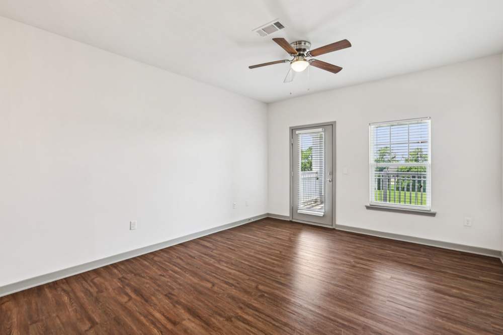 Empty living room with wood floors, ceiling fan, window, and door to patio at The Drake in Bowling Green, Kentucky  