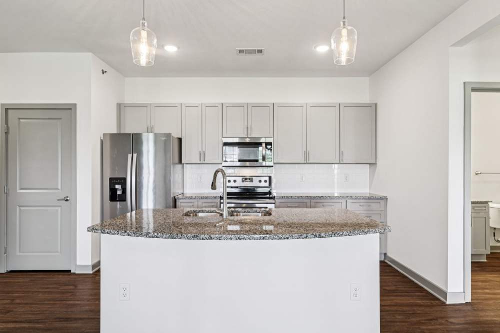 Kitchen with granite island, pendant lights, and gray cabinets along back wall at The Drake in Bowling Green, Kentucky  