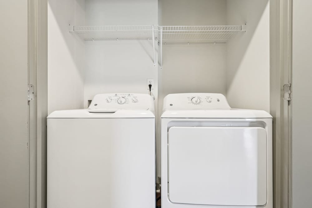 Laundry closet with white washer, dryer, and wire shelf above at The Drake in Bowling Green, Kentucky  