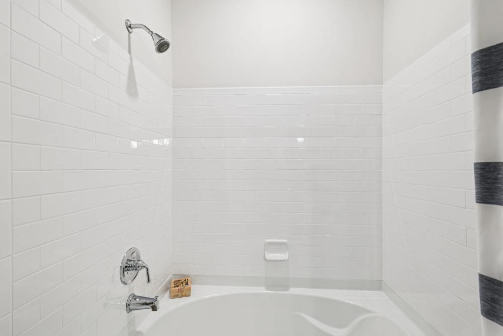 White-tiled bathtub and shower with chrome fixtures and striped curtain at side at The Drake in Bowling Green, Kentucky  
