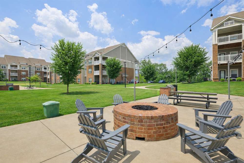 Brick fire pit area with Adirondack chairs and string lights near apartment buildings at The Drake in Bowling Green, Kentucky
