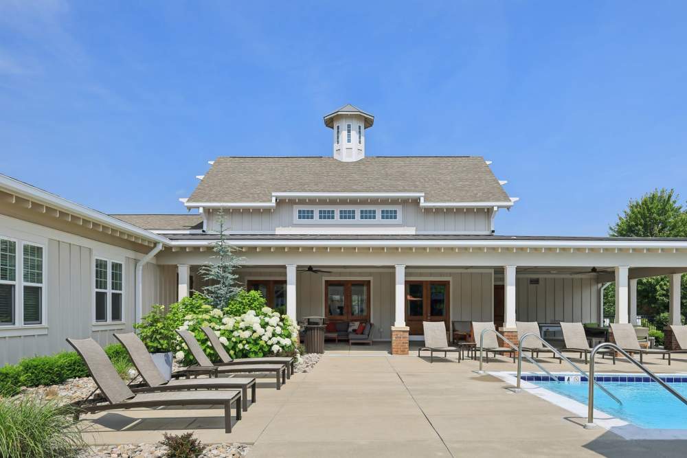 Clubhouse exterior with covered patio, lounge chairs, and landscaped plants beside the pool at The Drake in Bowling Green, Kentucky