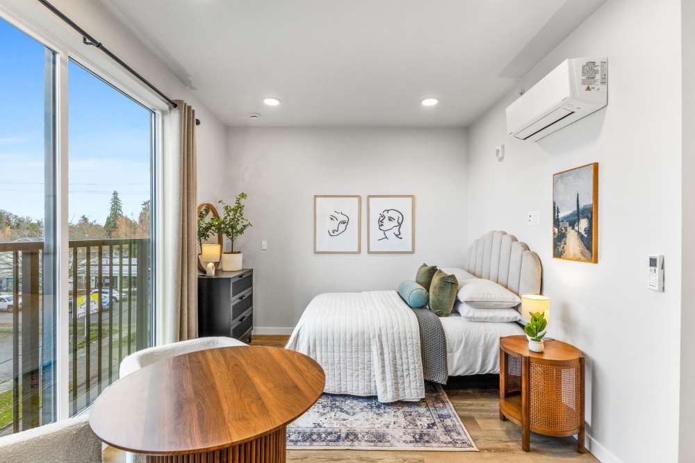 Studio bedroom with art, round table, and bright balcony window at Cartwright Apartments in Salem, Oregon