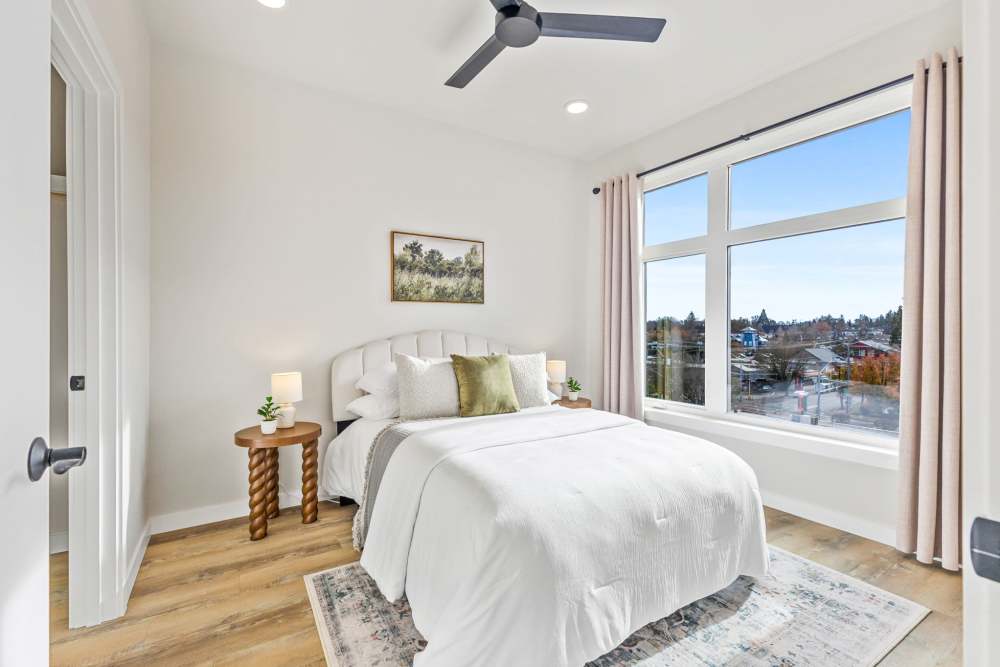 Bedroom with large window, ceiling fan, and neatly made bed at Cartwright Apartments in Salem, Oregon