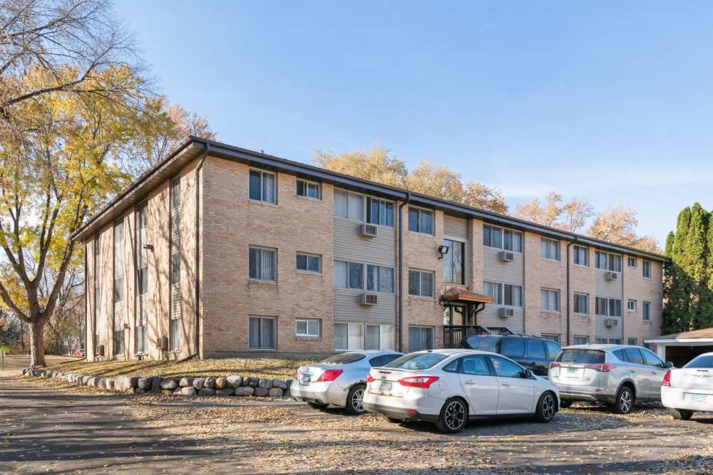 Exterior view of the apartment with surrounded by trees and parking cars at West End Trails in Golden Valley, Minnesota