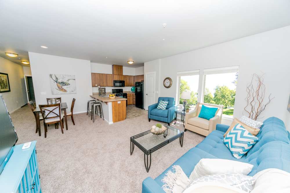 Open living room with blue seating, large windows, and view of kitchen at Columbia View in Vancouver, Washington