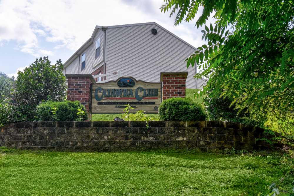Apartment community sign surrounded by greenery and landscaped bushes in a sunny setting at Catawba Club in Berkeley Springs, West Virginia