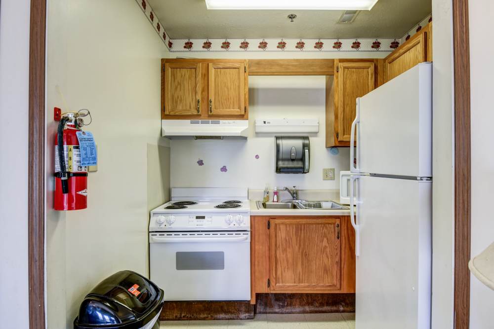 Compact clubhouse kitchen with white appliances, wooden cabinets, and a fire extinguisher on the wall at Catawba Club in Berkeley Springs, West Virginia