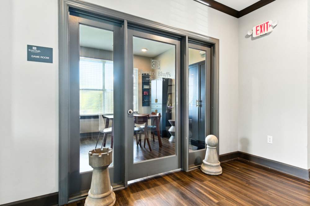 Game room entrance with wood-style flooring and large windows, featuring a table and chairs inside at Bristol Bluffs Apartments in Louisville, Kentucky