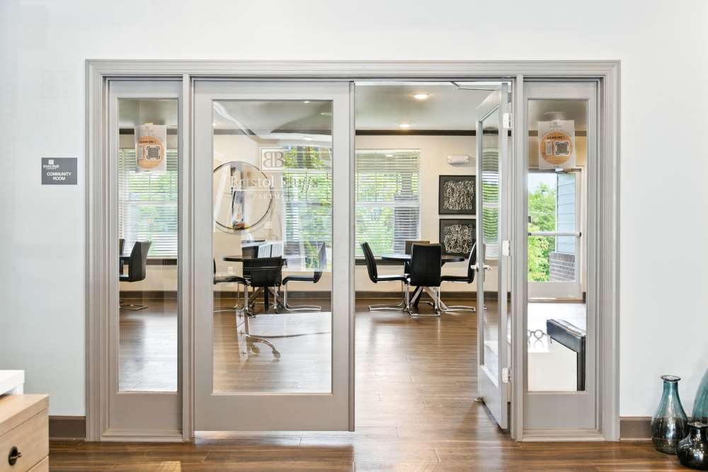 Modern community room with wood-style flooring and large windows, featuring a conference table and chairs at Bristol Bluffs Apartments in Louisville, Kentucky