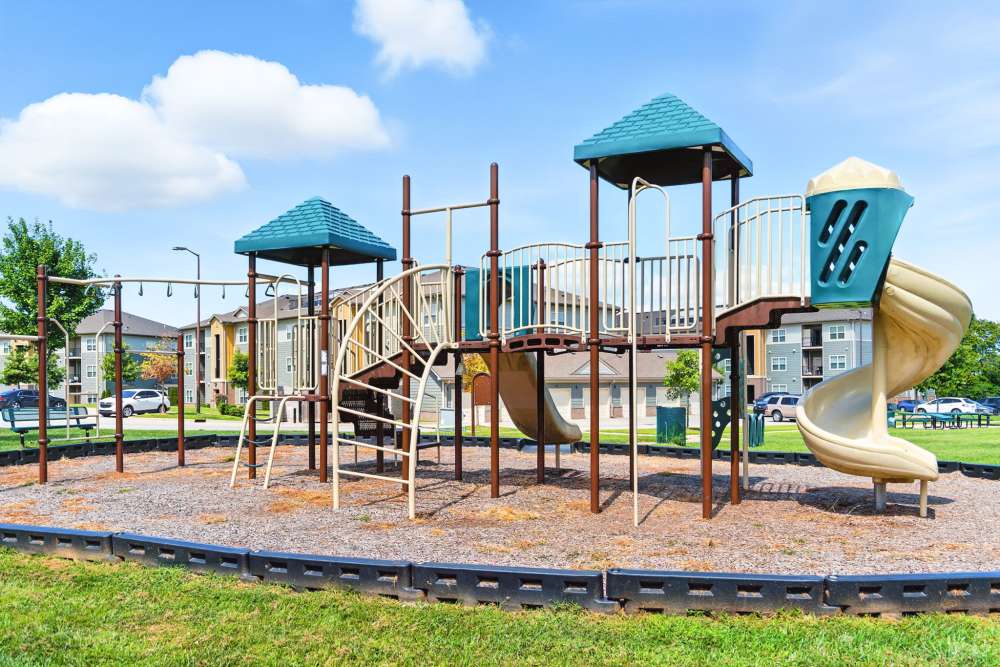 Colorful playground with slides and climbing structures in a grassy area near apartment buildings at Bristol Bluffs Apartments in Louisville, Kentucky