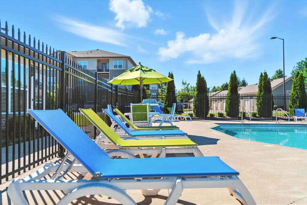 Resort-style pool area with lounge chairs and umbrellas, surrounded by a gated fence and greenery at Bristol Bluffs Apartments in Louisville, Kentucky