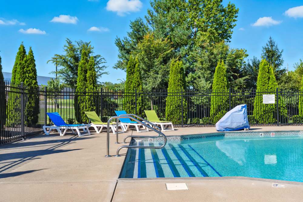Sparkling pool surrounded by lounge chairs and lush greenery in a gated community at Bristol Bluffs Apartments in Louisville, Kentucky