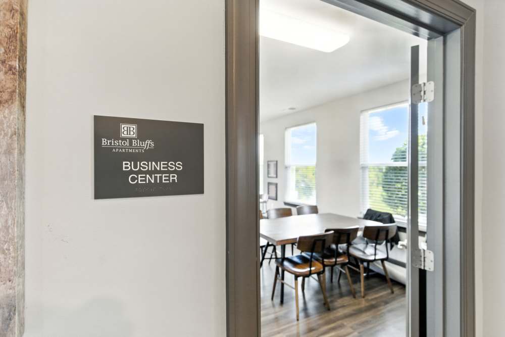 Bright business center with large windows, modern table, and stylish chairs on wood-style flooring at Bristol Bluffs Apartments in Louisville, Kentucky