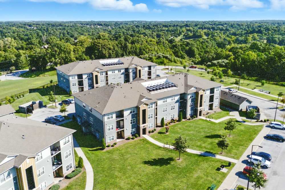 Aerial view of modern apartment community with green lawns and trees, featuring multiple buildings and parking areas at Bristol Bluffs Apartments in Louisville, Kentucky