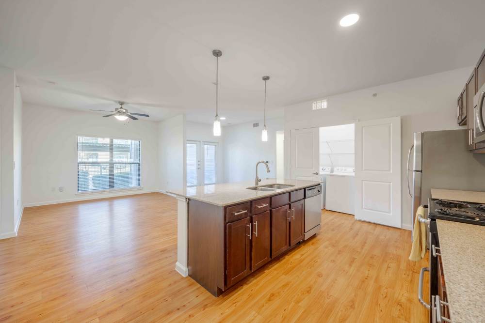 Spacious kitchen with hardwood flooring, central kitchen island, and open living room with large windows and abundant natural light in Austin, Texas.
