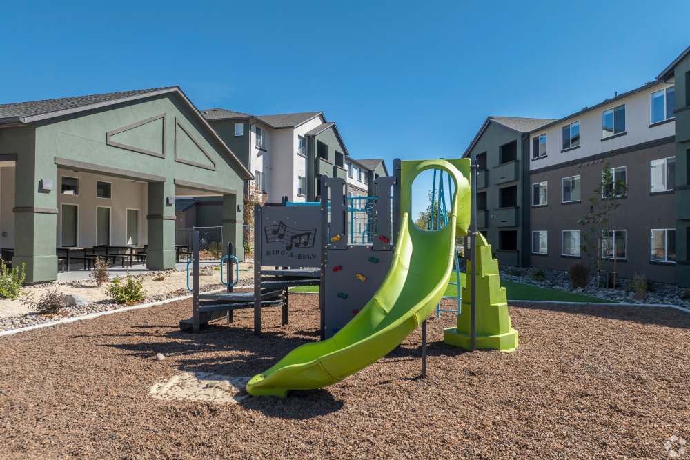Outdoor playground with green slide and play structures between apartment buildings at Sage by Vintage in Reno, Nevada