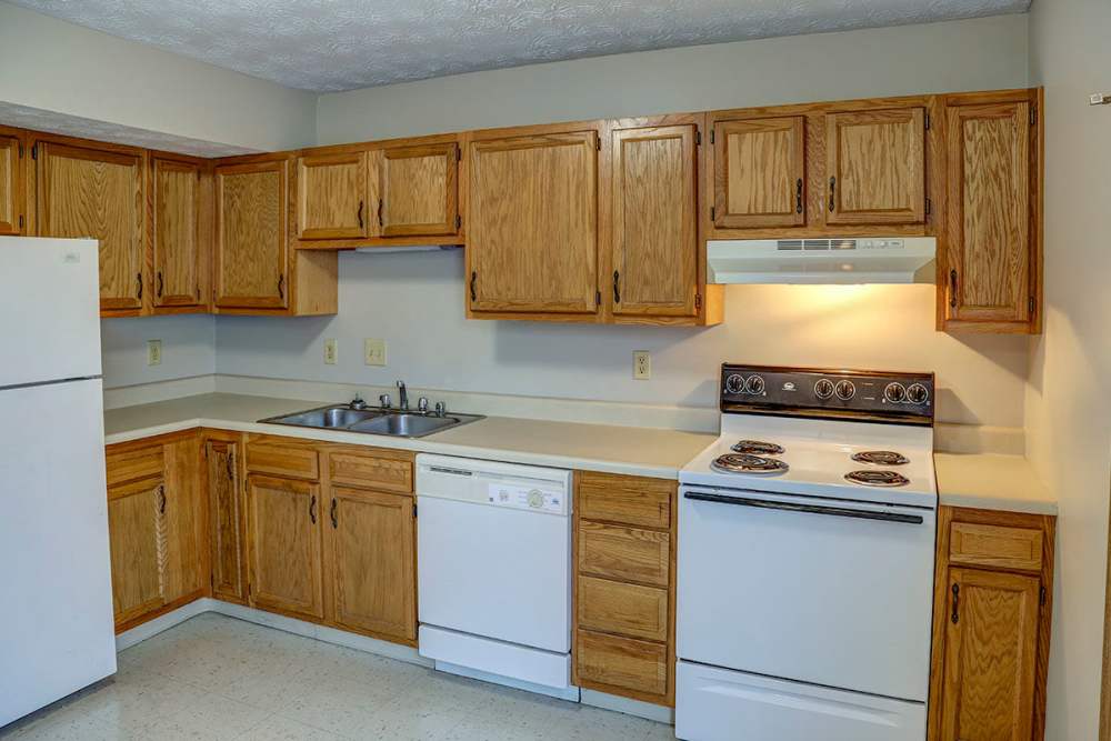 Bright kitchen with wooden cabinets, white appliances, and double sink on a light countertop at Arlington Terrace in London, Kentucky