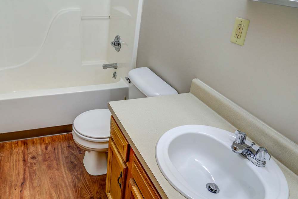 Bright bathroom with wood-style flooring, white sink, and bathtub with showerhead at Arlington Terrace in London, Kentucky