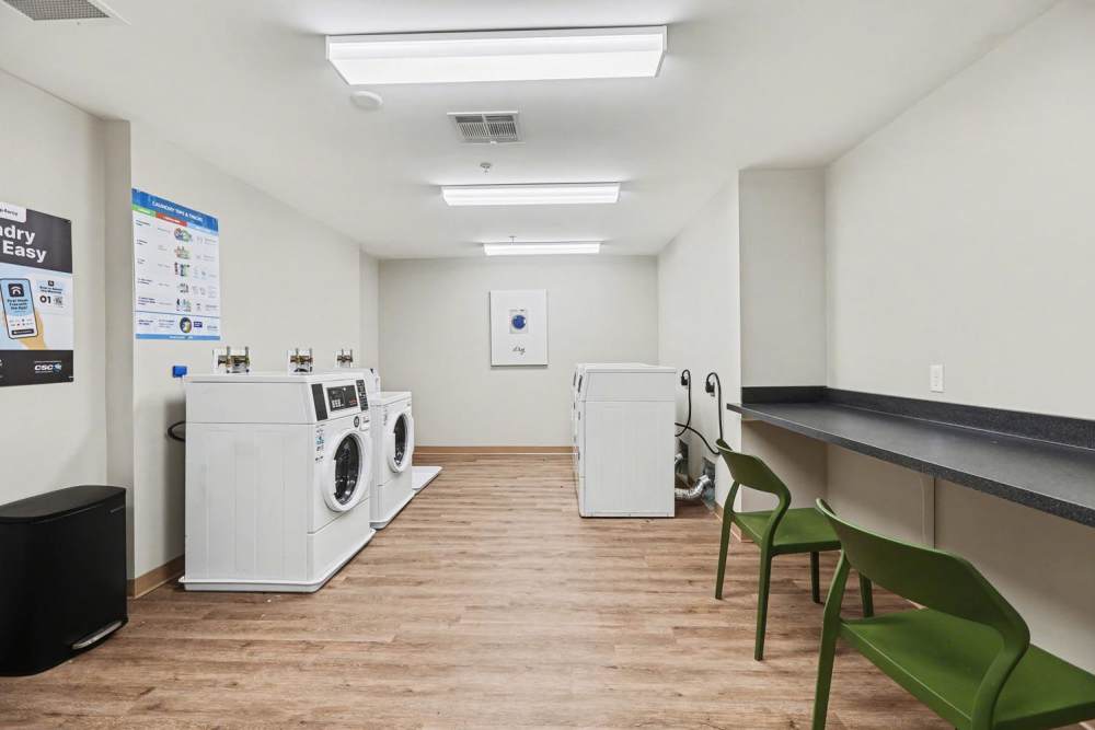 Bright laundry room with two washing machines, folding counter, and green chairs on wood-style flooring at Annika Place II in Traverse City, Michigan
