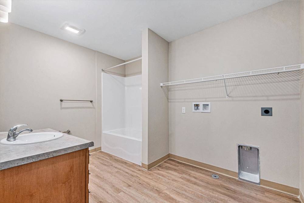 Spacious bathroom with wood-style flooring and a bathtub, featuring a sink and storage cabinet at Breton Grove II in Grand Rapids, Michigan