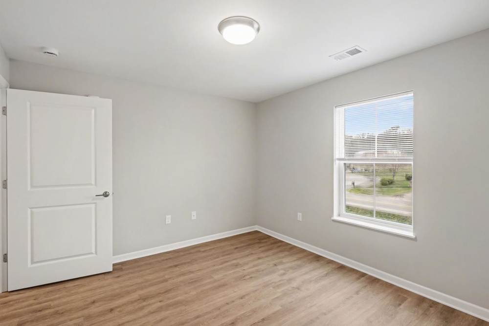 Bright room with wood-style flooring and large window, featuring a white door and neutral walls at Bridlewood Crossing in Louisville, Kentucky