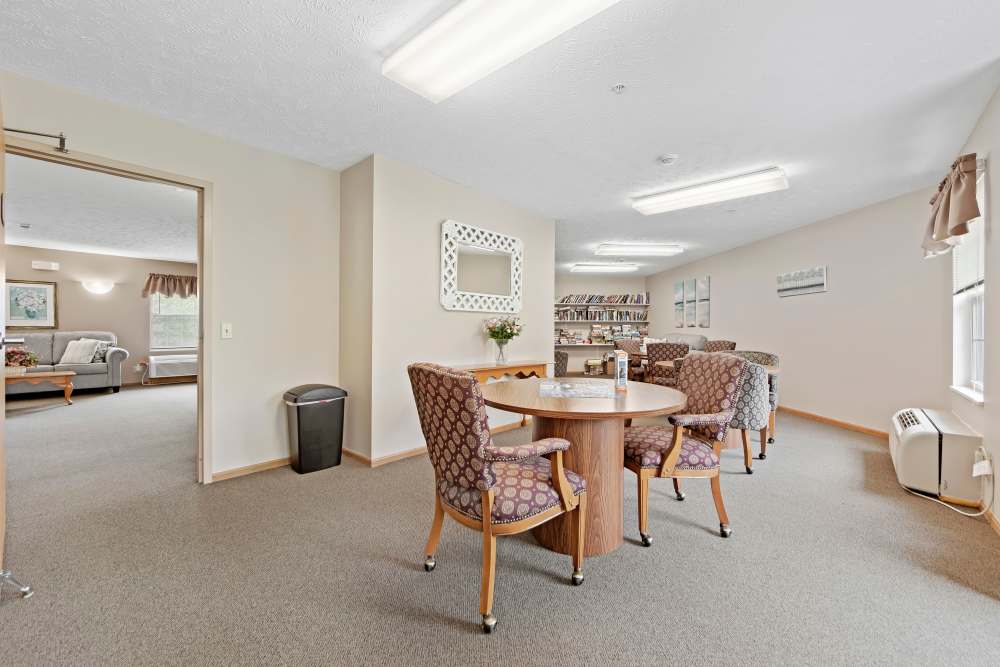 Community lounge with round table, patterned chairs, bookshelf, and cozy seating area at Heritage Village in Steubenville, Ohio