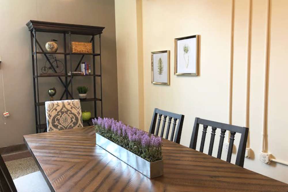 Modern dining area with wooden table, decorative flowers, and stylish chairs against a neutral wall at Lincoln House in Owosso, Michigan