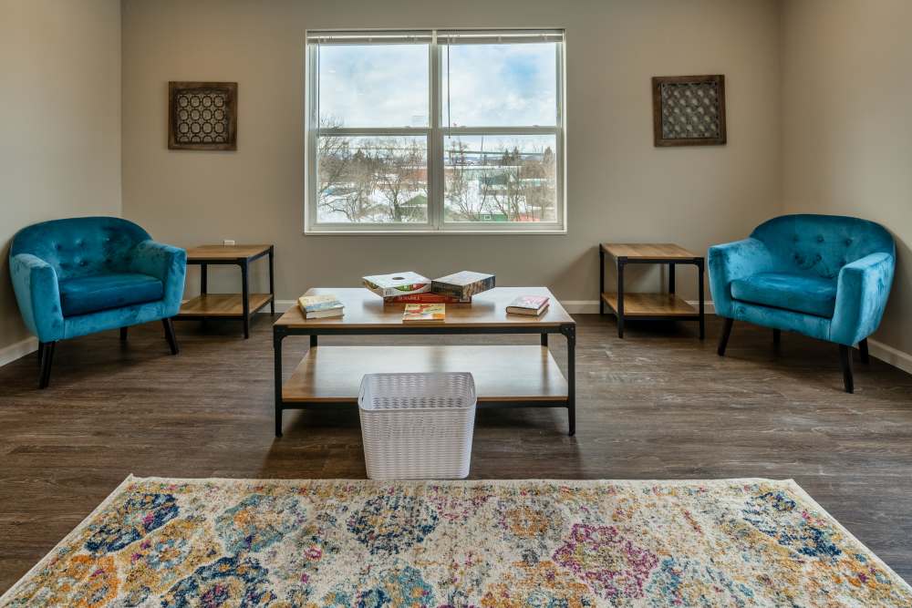 Bright living room with wood-style flooring, two teal chairs, and a coffee table with books at Osborn Commons in Sault Sainte Marie, Michigan