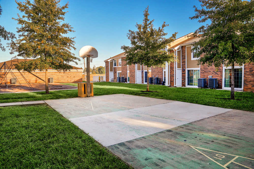 Basketball court with hoop, grassy area, and playground equipment in a pet-friendly apartment community at Mason Greene in Monticello, Kentucky