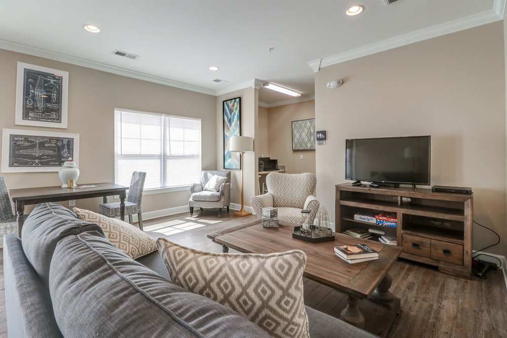 Cozy lounge with wood-style flooring, comfortable seating, and natural light from large windows at Oliver Crossing in Linden, Tennessee