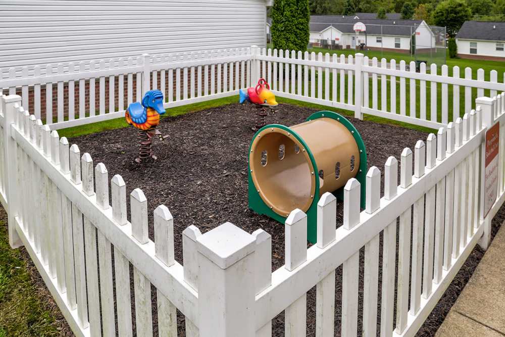 Colorful playground equipment in a fenced pet-friendly area with mulch flooring and white picket fence at Paint Landing in Stambaugh, Kentucky