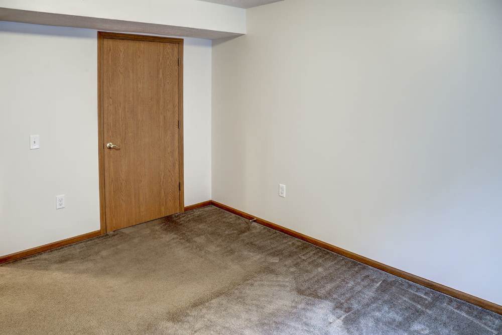 Empty room with beige carpet, wooden door, and light-colored walls, ready for personalization at Preston's Crossing in Prestonsburg, Kentucky