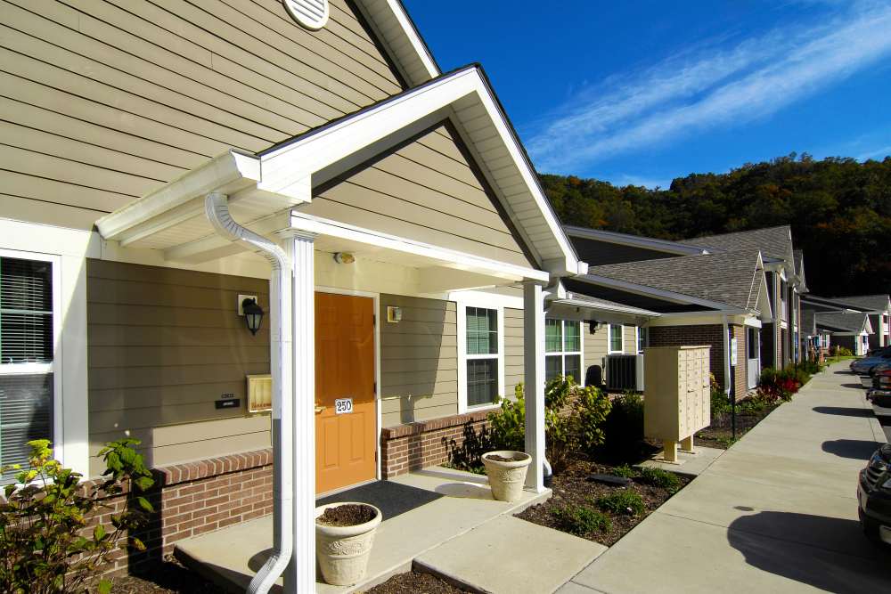 Welcoming entrance with a bright orange door, landscaped garden, and nearby parking spaces at Preston's Crossing in Prestonsburg, Kentucky