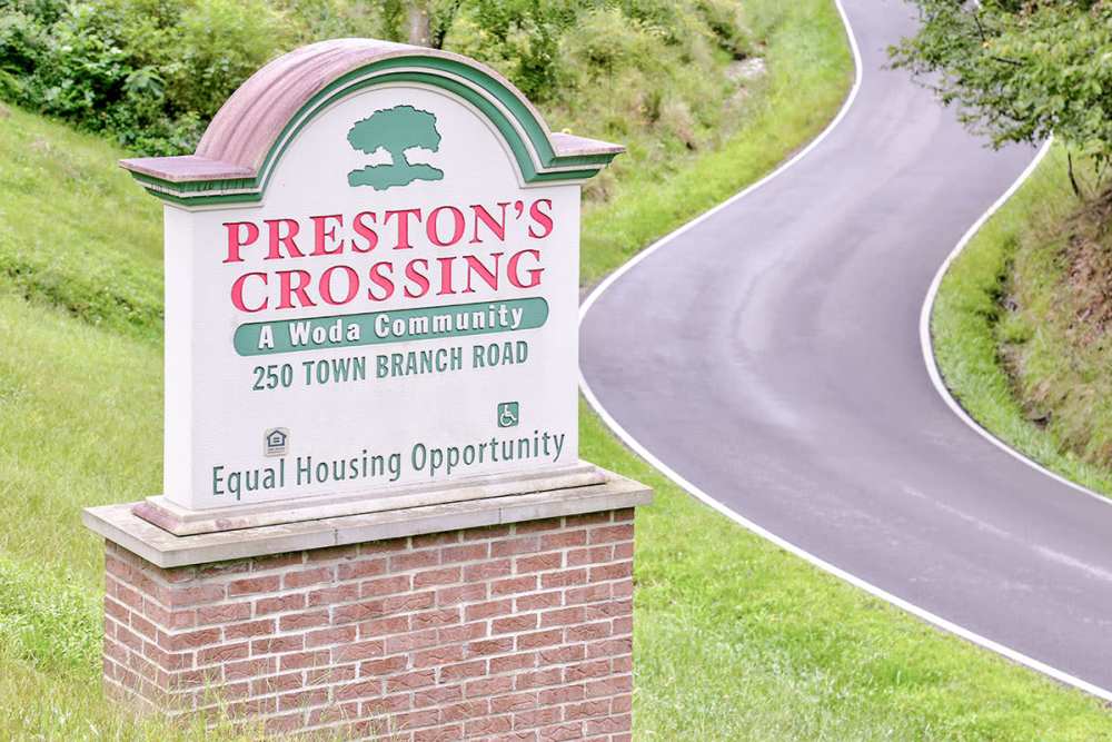 Community sign with green landscaping and winding road leading to apartment entrance at Preston's Crossing in Prestonsburg, Kentucky