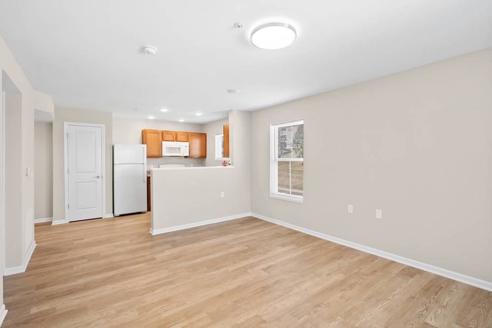 Open layout living area with wood-style flooring and kitchen featuring stainless steel appliances and wooden cabinets at Sparrow Ridge in Hebron, Kentucky