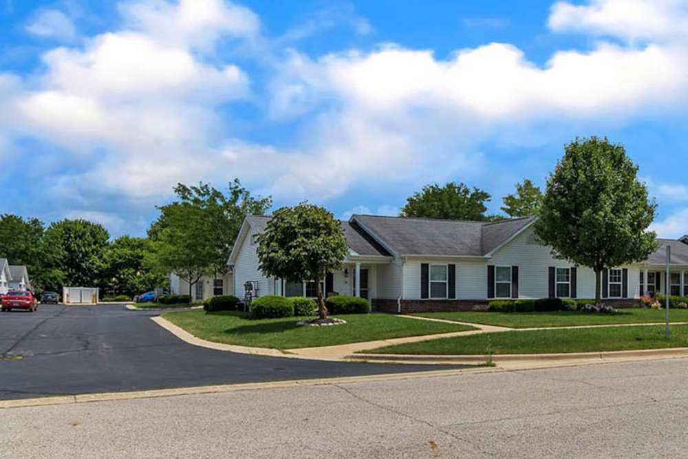 Charming apartment community with well-maintained landscaping and inviting walkways under a bright blue sky at Tibbits Greene Senior Living in Coldwater, Michigan