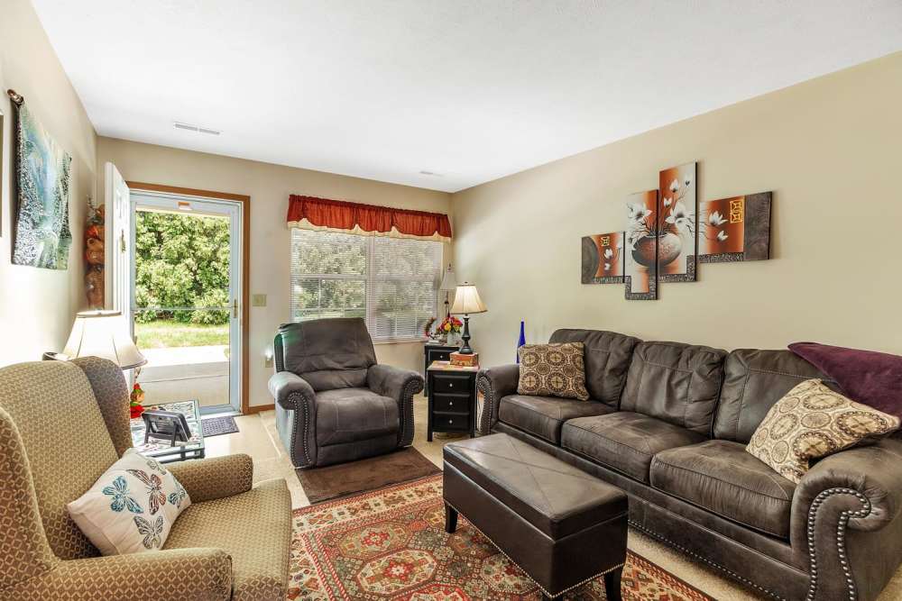 Cozy living room with leather sofa, patterned rug, and natural light from the door and windows at Tibbits Greene Senior Living in Coldwater, Michigan