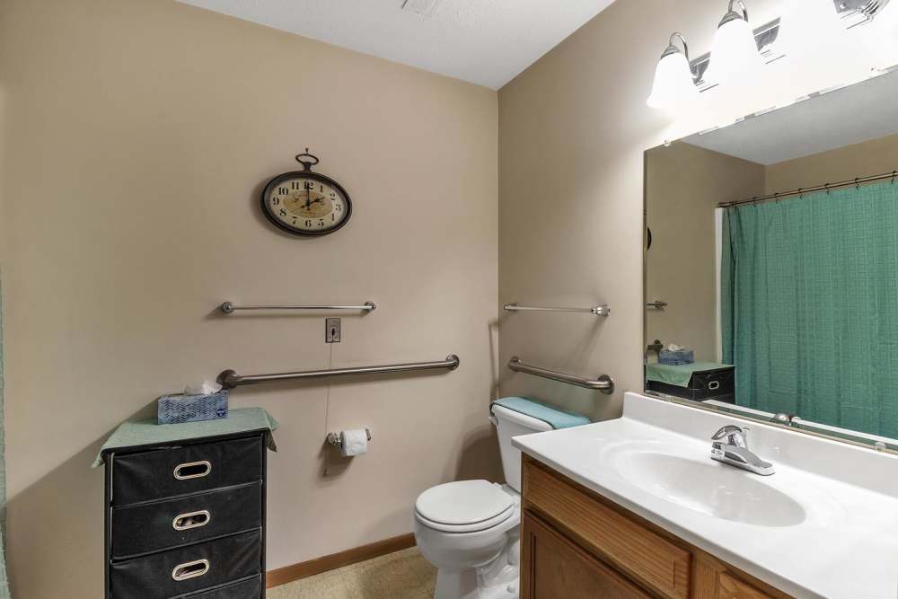Bright bathroom with a large mirror, wooden vanity, and teal shower curtain at Tibbits Greene Senior Living in Coldwater, Michigan
