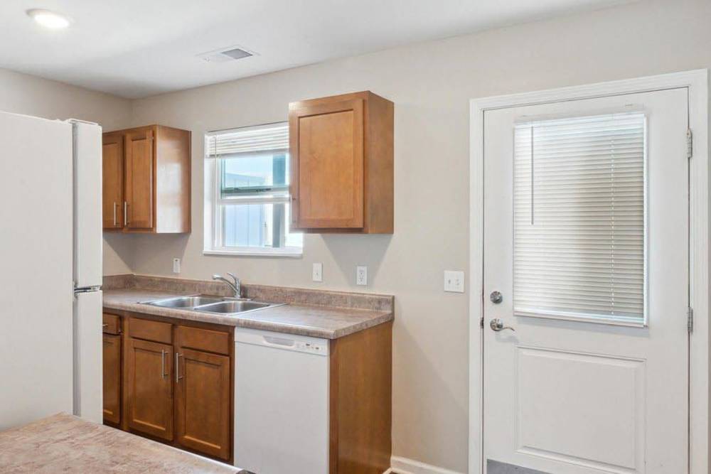 Modern kitchen with wooden cabinets, stainless steel appliances, and double sink near a door to the outside at Winston Commons in Pontiac, Michigan