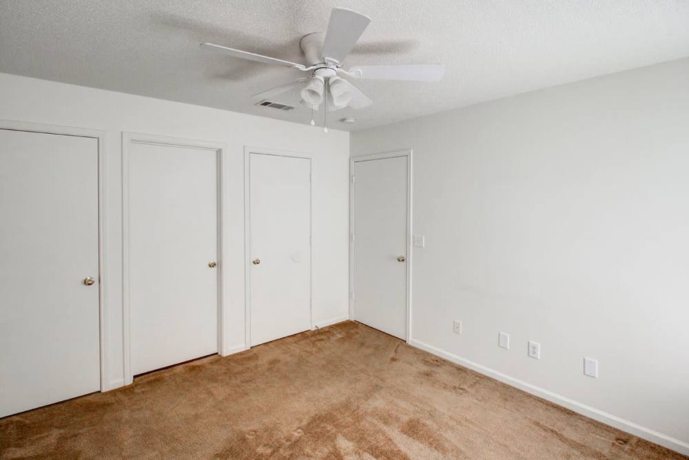 Empty bedroom with beige carpet, ceiling fan, and three white doors on the wall at Valley View Gardens in Dunlap, Tennessee