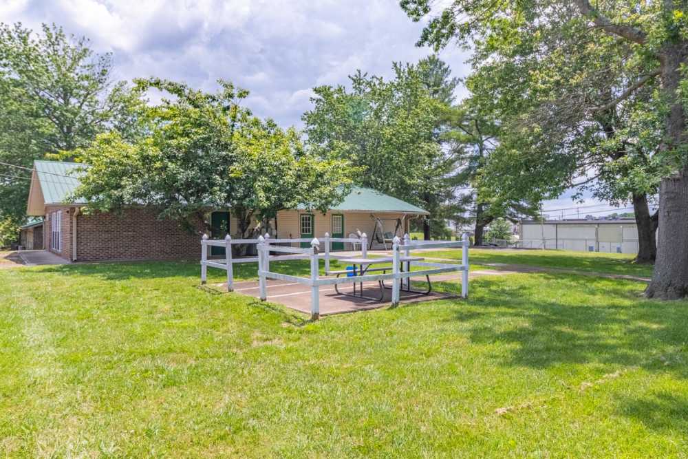Gated outdoor area with picnic tables and shaded trees in a grassy setting at Walnut Street Apartments in Dickson, Tennessee