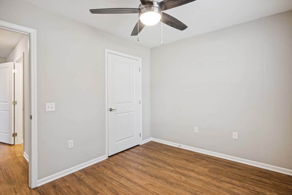 Empty bedroom with wood-style flooring and ceiling fan, light gray walls, and white doors at Woodbury Crossing in Corryton, Tennessee
