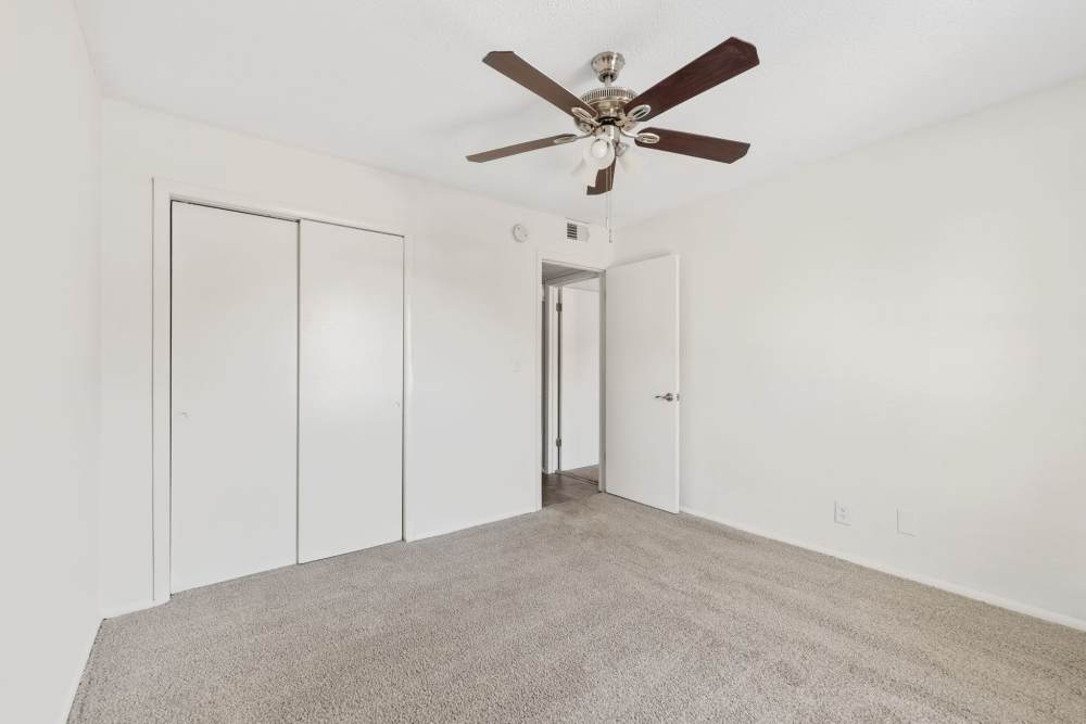 Empty bedroom with light carpet, white walls, ceiling fan, sliding closet doors, and open doorway at Palmetto Square in Charleston, South Carolina  