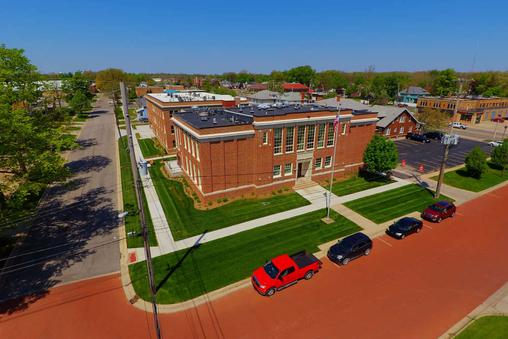 Aerial view of a brick building surrounded by green lawns and parked cars on a sunny day at Lincoln House in Owosso, Michigan