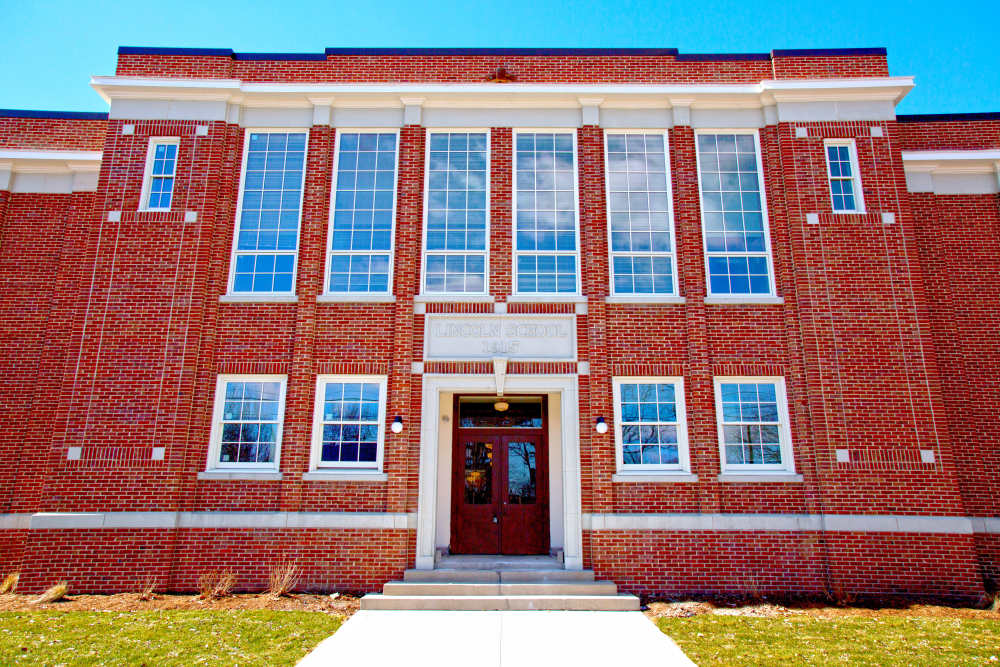 Brick building with large windows and a welcoming entrance surrounded by green grass at Lincoln House in Owosso, Michigan