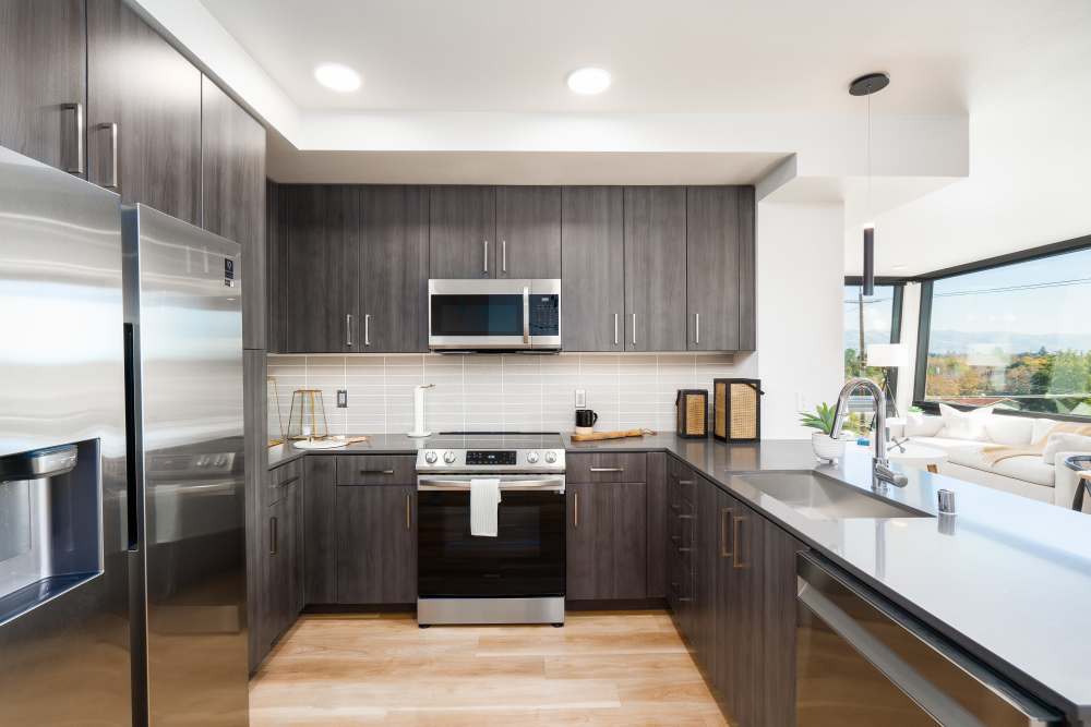 Modern kitchen featuring stainless steel appliances, granite countertops, and wood-style flooring at Exhibit at J Town in San Jose, California